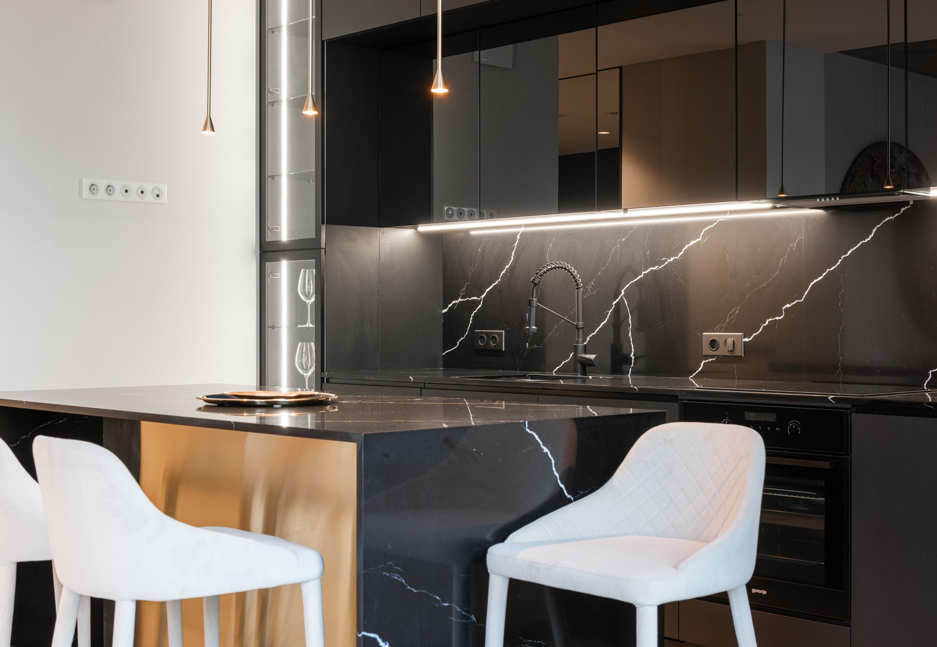 Interior of modern kitchen with white chairs near counter and black cabinets with oven near faucet with sink in Austin, TX